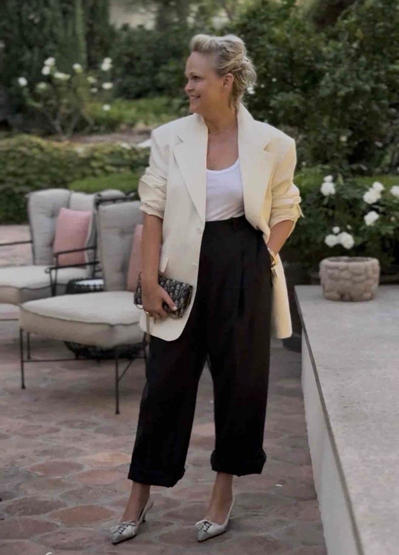 Tiffany in a cream blazer with a white top, black trousers and a patterned clutch