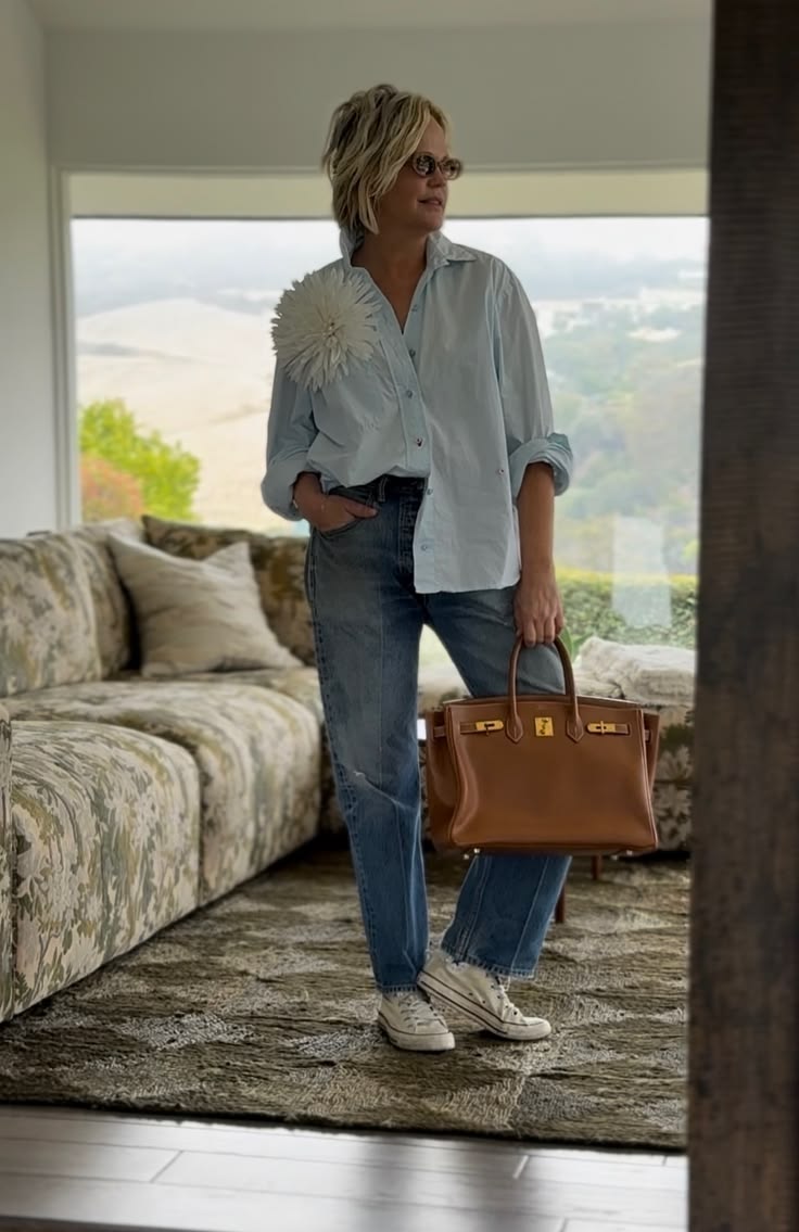 Tiffany wearing a light blue floral shirt, jeans, Converse, and a tan leather bag